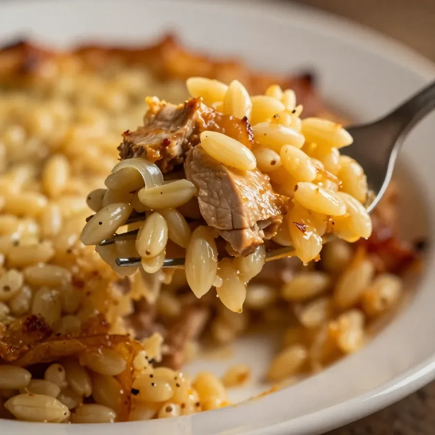 A close-up of French Onion Chicken Orzo Casserole in a baking dish topped with melted cheese and fresh herbs.